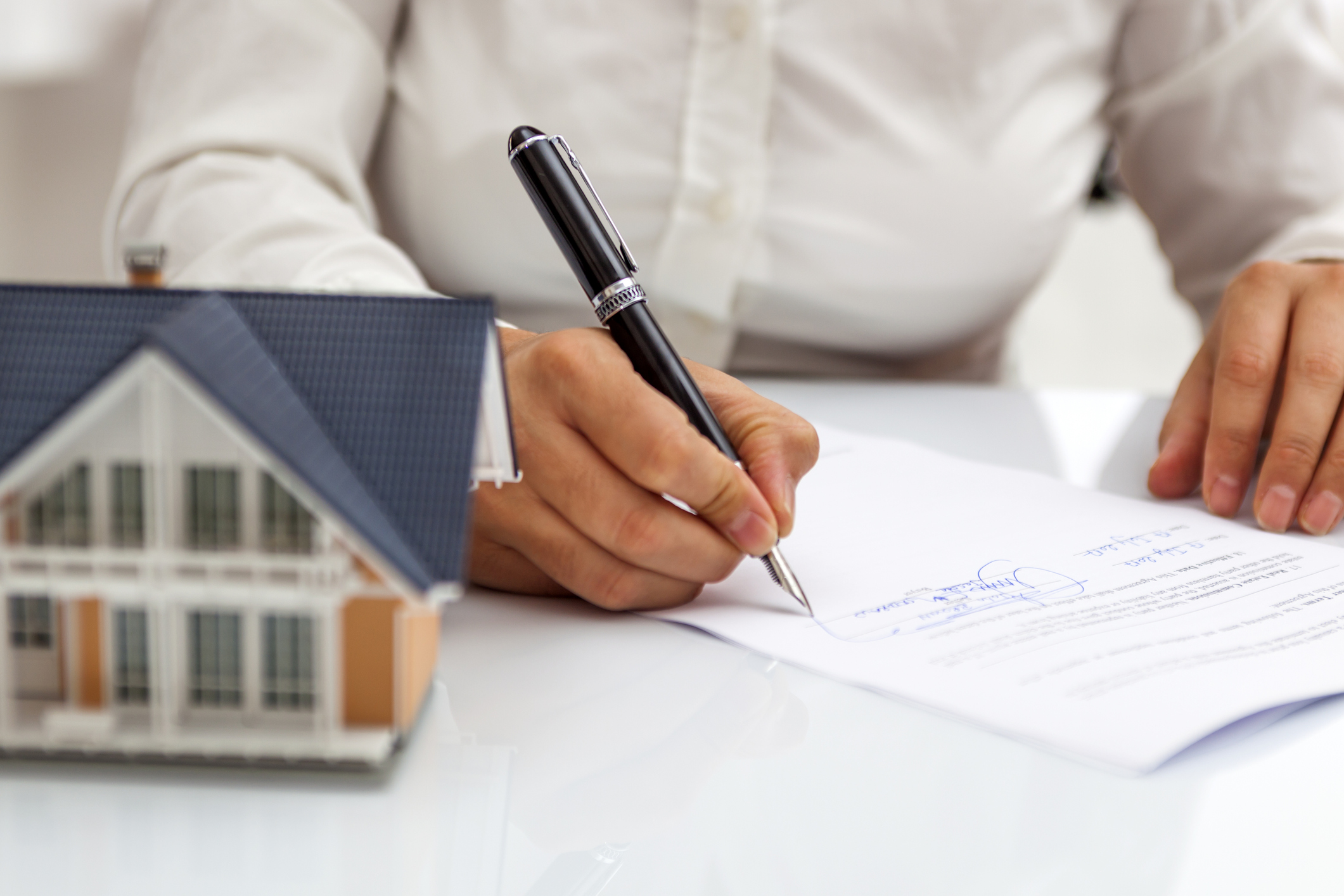 close up of person signing a leasing document next to a model house